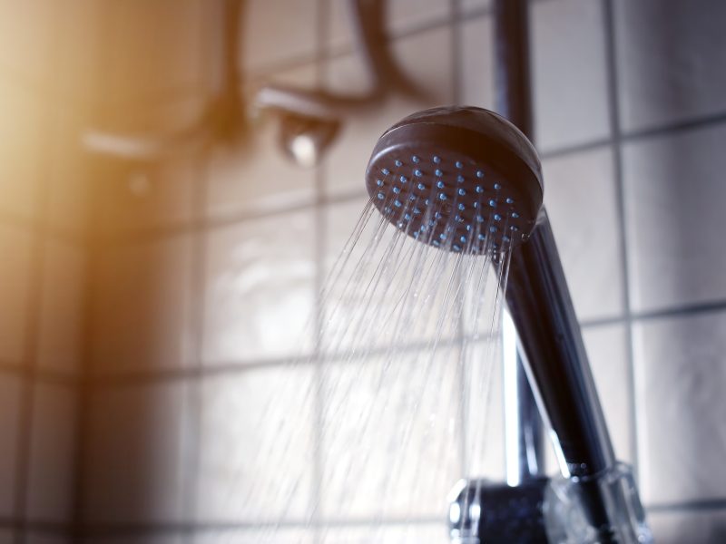 Shower head with running water in a bathroom with morning sun light. Take a bath in morning time.